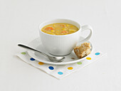 Corn chowder in teacup on saucer with bread and spoon