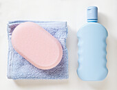 Shampoo, folded blue towel and pink bath sponge