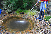 Person filling garden pond with water from hose
