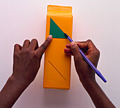Child's hands drawing around triangular shape on carton
