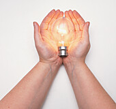 Two hands holding a lit light bulb