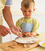 Boy and woman coating salmon fishcakes in flour
