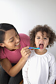 Woman holding toothbrush to girl's opened mouth