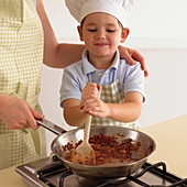 Boy stirring tomato sauce in saucepan