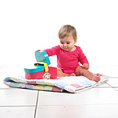 Baby girl sitting on quilt playing with toy picnic basket