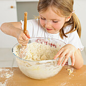 Girl holding bowl of cake mixture and wooden spoon