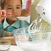 Boy adding a spoon of sugar to whisked egg white mixture