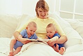 Woman sitting in bed reading to twins