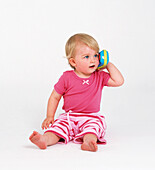 Baby girl holding plastic telephone toy to her ear