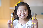 Girl holding knife, fork and spoon with yellow handles