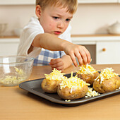 Boy placing cheese on jacket potato