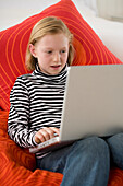 Girl sitting on red cushions using laptop