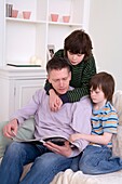 Man and two boys sitting on sofa looking at brochure