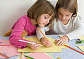 Twin girls drawing together on sheets of coloured paper
