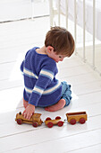 Boy kneeling on floor pushing wooden toy