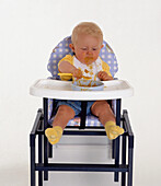 Baby boy learning to feed himself sitting in highchair