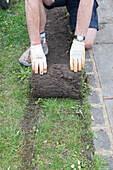 Person rolling up a strip of turf by a garden path