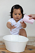 Baby girl watching as woman pours water from cup into bowl