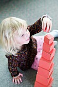 Girl stacking red wooden blocks in size order
