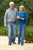Older woman supporting man as they walk through garden