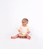 Baby girl sitting on floor playing with toy drum