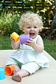 Baby girl in garden holding plastic cups