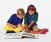 Girl and boy sitting on floor looking at photo album
