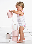 Toddler girl in underwear stacking toilet rolls