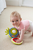 Baby girl crawling on carpet with soft toy