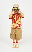 Boy in safari-style clothes looking through binoculars