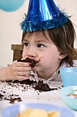 Boy wearing party hat eating crumbly chocolate cake