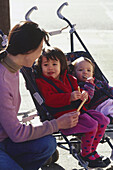 Woman kneeling next to girls strapped into double pushchair