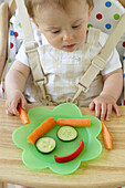 Baby boy sitting in highchair looking at vegetables