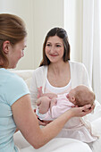 Smiling mother handing baby girl to friend