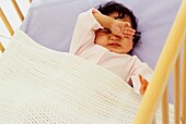 Baby lying in cot rubbing her eyes