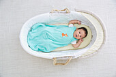 Baby boy in a sleeping bag in a Moses basket