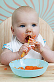 Baby boy in high chair eating pureed food with spoon