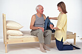 Woman dressing a man sat on the side of a bed