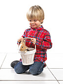 Young boy holding rabbit in wooden bucket