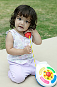 Baby girl in garden playing with plastic toy telephone