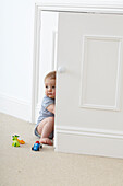 Baby boy sitting on carpet near open cupboard door