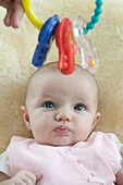 Baby girl lying down and looking at plastic rattle toy