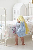 Baby boy standing next to bed with blanket over his head