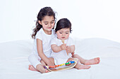 Baby girl and older sister playing with toy xylophone