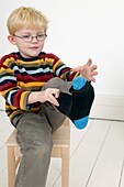 Boy seated on chair putting on a sock