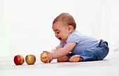 Baby boy picking up apple with both hands