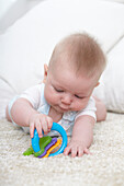 Baby boy playing with teething ring on carpet