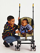 Boy crouching next to baby boy in pushchair