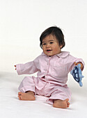 Baby sat on the floor wearing pink check pyjamas