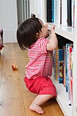 Baby girl pulling herself up on bookshelf